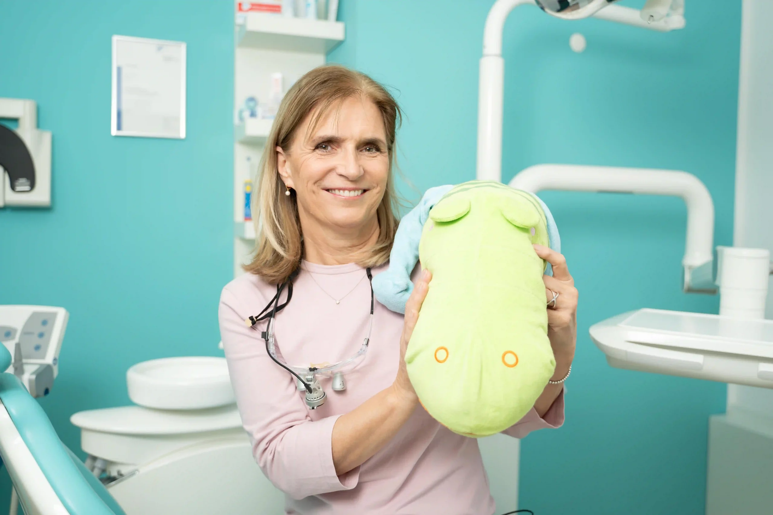 Dr. Ulrike Uhlemann hält im Behandlungszimmer ein grünes Plüschtier für die kleinen Patienten